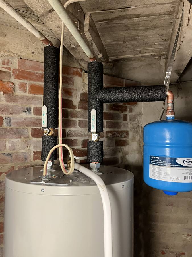 Close-up of insulated hot and cold lines with shut-off valves and a blue expansion tank