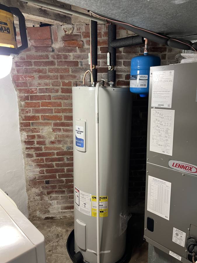New Bradford White electric water heater against a brick wall beside an air handler