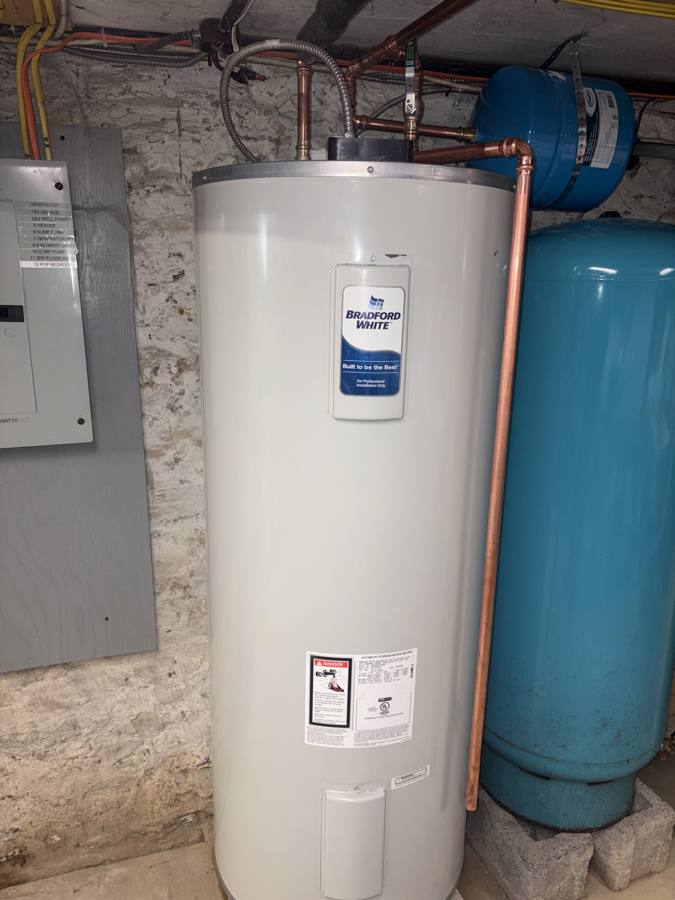 New Bradford White electric water heater in the same stone basement, with new copper piping