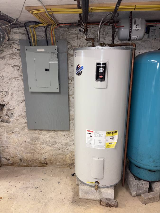 Old electric water heater on a cinder block in a stone basement, before replacement